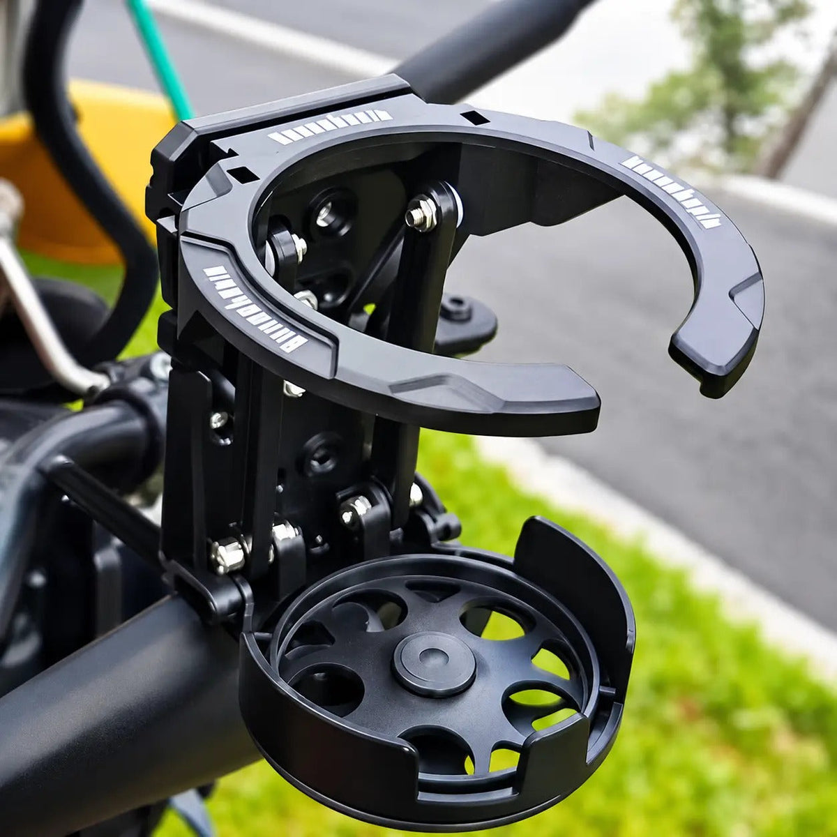 The black RideCup drink holder mounted on a motorcycle handlebar in the open position.